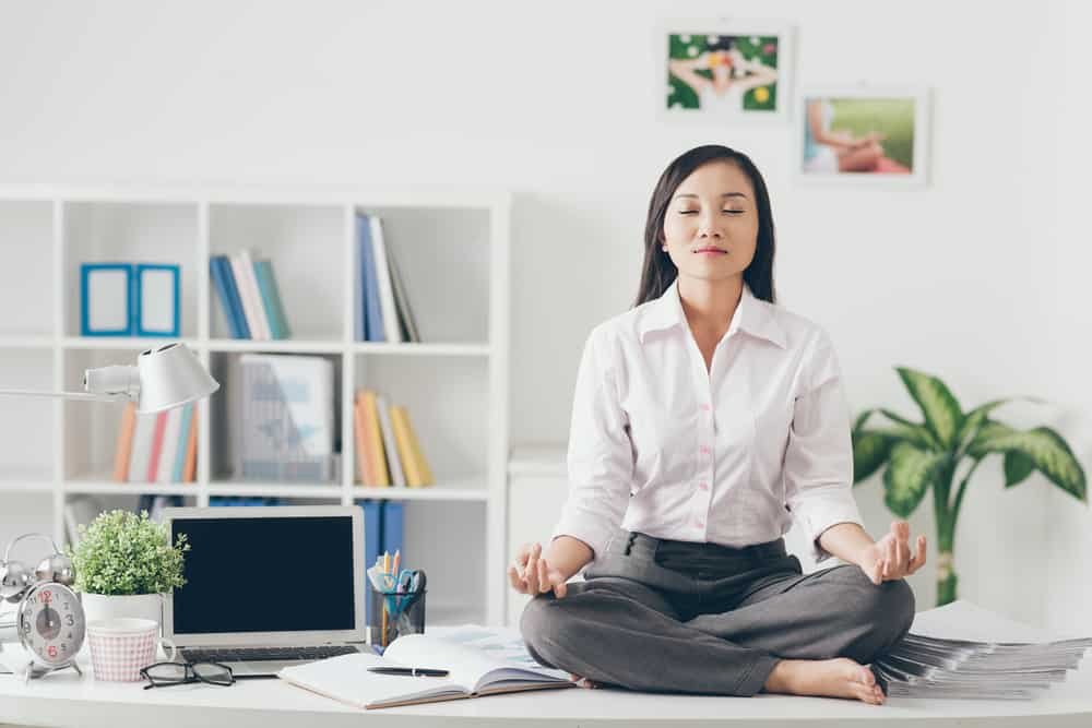 Female office worker meditating on her work place yoga